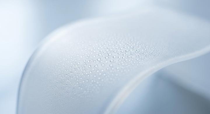 Abstract close-up of water-resistant polymer material with micro condensation droplets under soft laboratory lighting