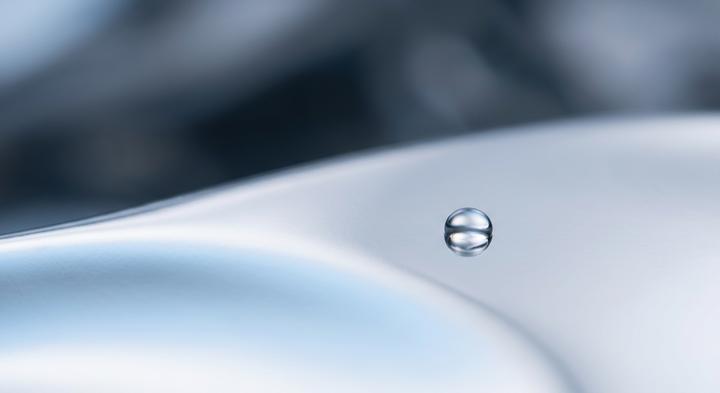 Abstract macro shot of a clean metallic surface reflecting a single tiny dew droplet representing chilled-mirror technology