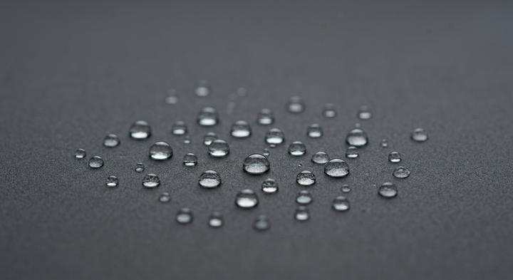 Water droplets beading on a dark grey hydrophobic surface representing humidity protection